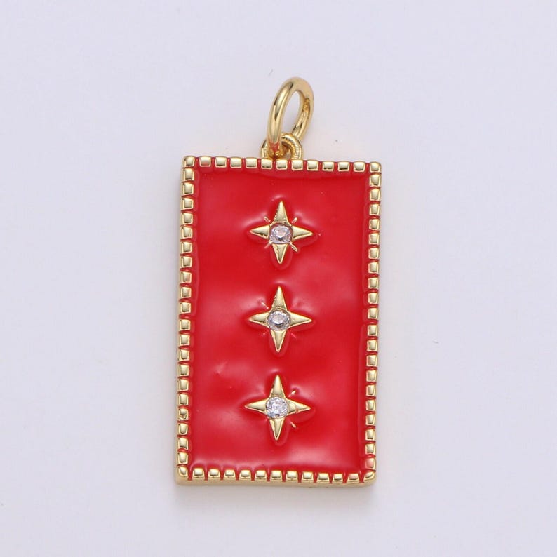 May include: A gold pendant with a red enamel rectangle featuring three gold stars with clear rhinestones. The pendant has a gold border with a repeating pattern.