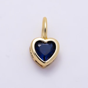 May include: A gold heart-shaped pendant featuring a deep blue gemstone set in the center. The pendant has a smooth, polished gold frame and a small gold bail at the top for attachment to a chain, showcasing a classic and elegant jewelry design.