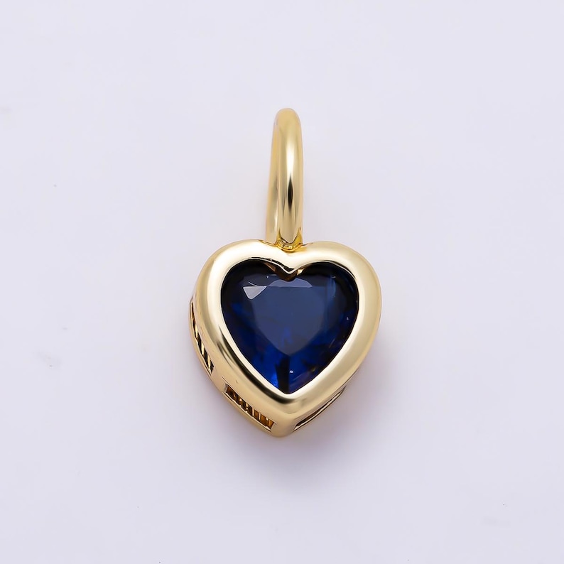 May include: A gold heart-shaped pendant featuring a deep blue gemstone set in the center. The pendant has a smooth, polished gold frame and a small gold bail at the top for attachment to a chain, showcasing a classic and elegant jewelry design.