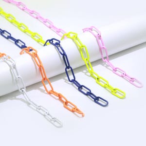 May include: Five colorful plastic chains in white, orange, blue, yellow, and pink. The chains are made of linked oval shapes.