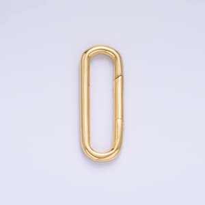 May include: A gold-colored, elongated oval clasp. The clasp is a single piece with a hinged opening on one side. The metal has a polished finish, reflecting light. The background is a solid, light color.