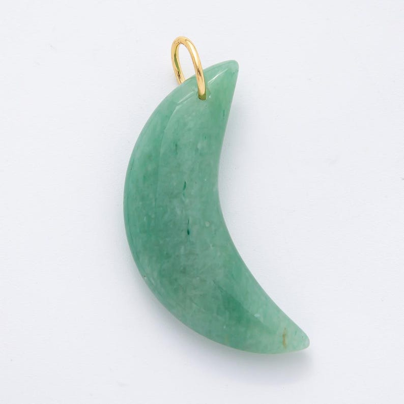 Op de afbeelding: Een maanvormige hanger van groene jade met een goudkleurige balein. De jade heeft een glad, gepolijst oppervlak en is licht doorschijnend. De hanger is ontworpen om als ketting te worden gedragen.