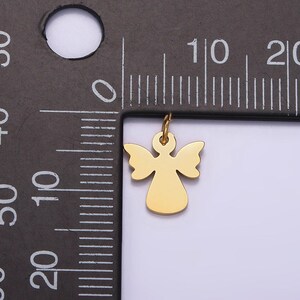 May include: A gold-colored angel charm pendant with a loop for attaching to a necklace or bracelet. The charm is about 1 cm in size and is shown next to a ruler.