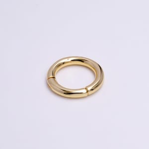 May include: A gold-colored metal ring with a smooth, rounded surface. The ring is open and has a hinged closure.