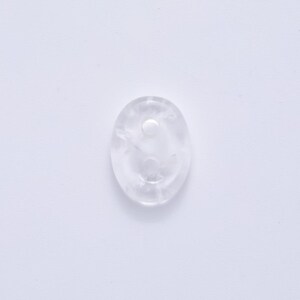 May include: A clear, oval-shaped crystal with a smooth surface. The crystal has a small, circular indentation on its surface. The crystal is translucent and appears to be made of quartz.