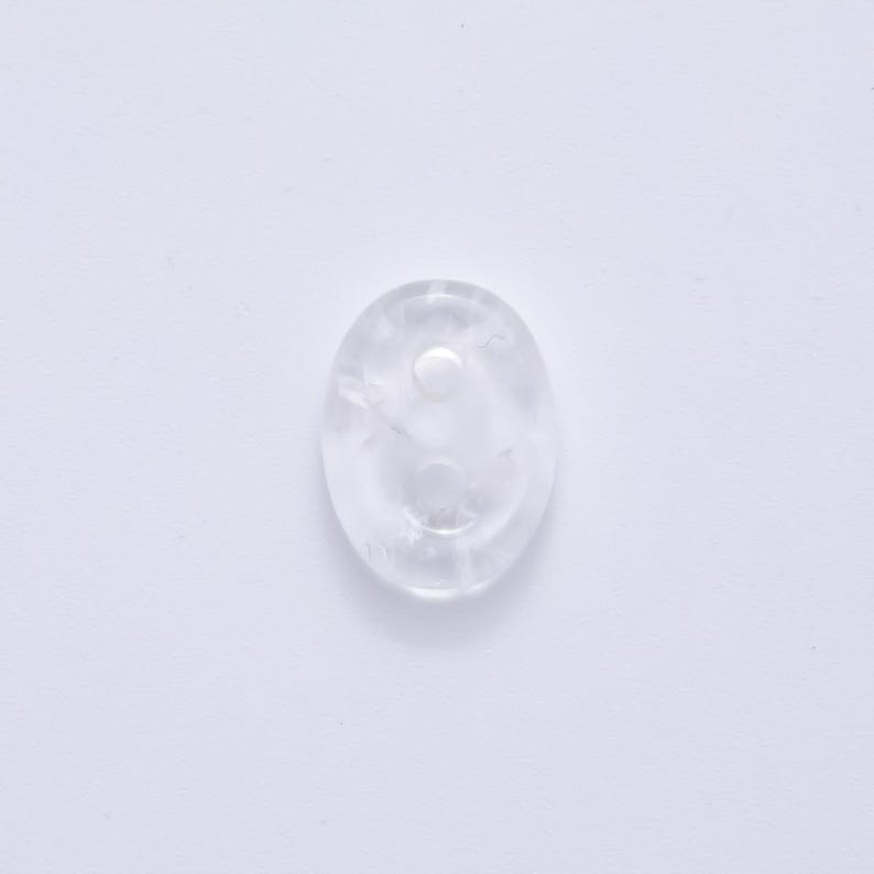 May include: A clear, oval-shaped crystal with a smooth surface. The crystal has a small, circular indentation on its surface. The crystal is translucent and appears to be made of quartz.