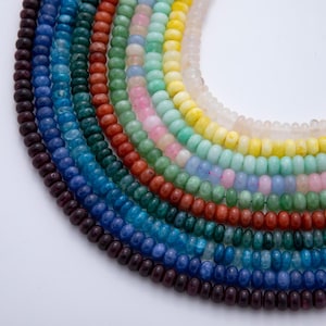 May include: Multiple strands of small, round, smooth gemstone beads arranged in a curved, rainbow-like gradient. The colors transition from deep purple and blue to green, orange, pink, light blue, yellow, and translucent white, creating a spectrum.