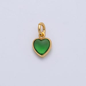 May include: A gold-colored heart-shaped pendant with a vibrant green center. The pendant has a small loop at the top for attaching to a chain or bracelet. The heart is outlined in gold, creating a striking contrast with the green gemstone.