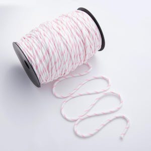 May include: A spool of white and pink striped rope. The rope is wound around a black plastic spool. A length of the rope is unraveled and lies on the white surface. The rope has a soft, flexible appearance.