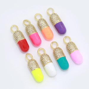 May include: Eight gold pill charms with clear rhinestones and colorful enamel. The charms are in the following colors: red, pink, orange, purple, turquoise, white, yellow, and light pink.