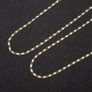 May include: Two gold chains with a diamond-shaped pattern. The chains are laid out on a black surface.