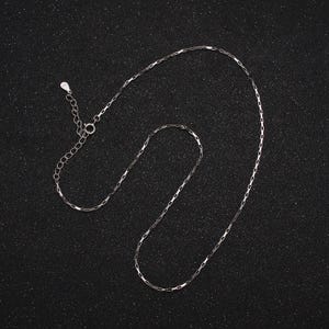 Puede incluir: Un collar de cadena de plata con cierre de mosquetón. La cadena está hecha de pequeños eslabones rectangulares.