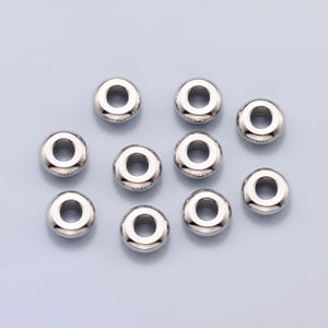 May include: A collection of ten shiny, silver-colored metal beads. Each bead is round with a hole through the center, and they are scattered on a light blue background. These beads are suitable for jewelry making and crafting.