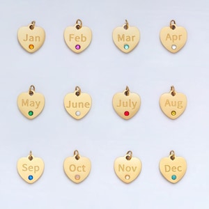 May include: Twelve gold heart-shaped charms with a different month of the year engraved on each charm. Each charm has a small gemstone in the center, representing the birthstone for that month.