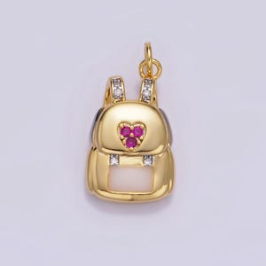 May include: A gold charm in the shape of a backpack with a heart-shaped ruby accent and clear crystal accents.