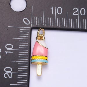 May include: Gold-tone charm shaped like a pink, white, and blue popsicle with a yellow stripe. The charm is about 2 inches tall.