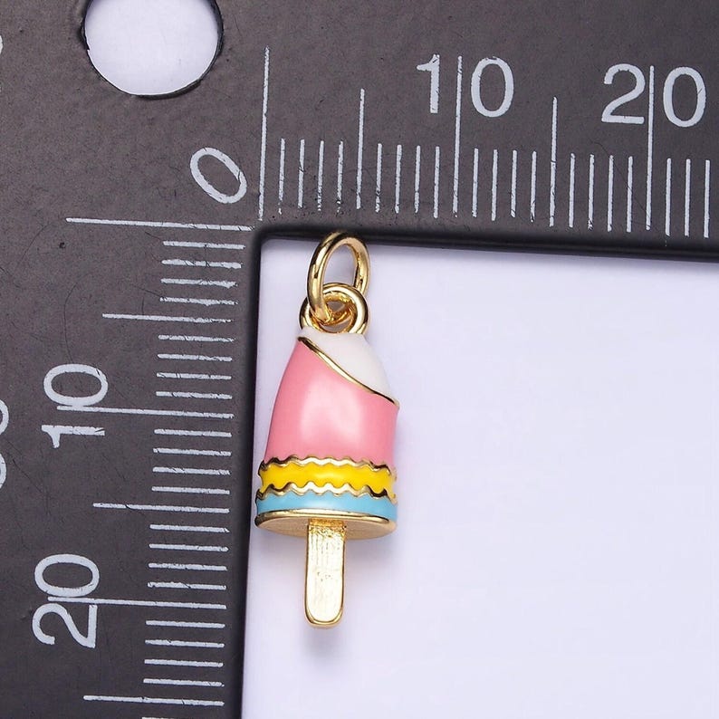 May include: Gold-tone charm shaped like a pink, white, and blue popsicle with a yellow stripe. The charm is about 2 inches tall.