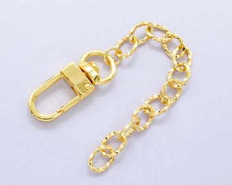 Pode incluir: Uma corrente de metal dourado com um fecho giratório. A corrente é torcida e tem um design decorativo. O fecho é preso a um laço em uma extremidade da corrente.