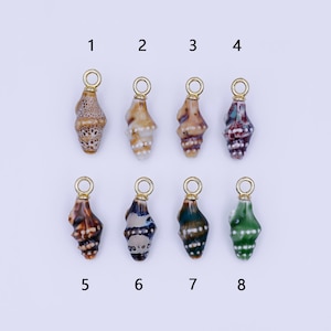 以下が含まれることがあります： 金色のループが付いた、ジュエリー作りに使用する8つの貝殻チャーム。チャームの色は、茶色、タン、青、緑、マルーンなど様々です。各チャームは、ユニークなパターンと質感を持っています。