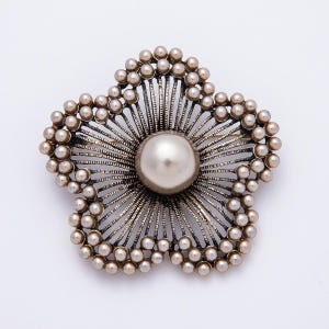 May include: A flower-shaped brooch featuring a large, central, lustrous pearl surrounded by radiating dark metal wire petals. The outer edges of the five petals are lined with numerous small, round, cream-colored faux pearls.