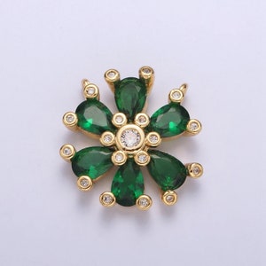May include: A gold-toned floral pendant featuring six emerald-green teardrop-shaped stones arranged around a central clear stone. Small clear stones accent each petal and the outer edges.