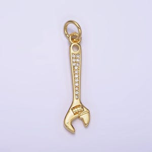 May include: A gold-toned wrench charm with clear sparkling stones. The wrench has a loop at the top for attaching to a chain or bracelet.