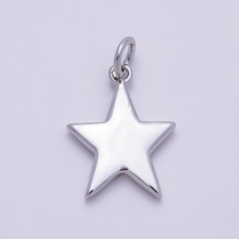 Puede incluir: Un colgante en forma de estrella de color plateado pulido con una superficie lisa y reflectante. La pieza tiene una forma sencilla de cinco puntas e incluye una peque&ntilde;a anilla circular en la parte superior para poder colgarla.