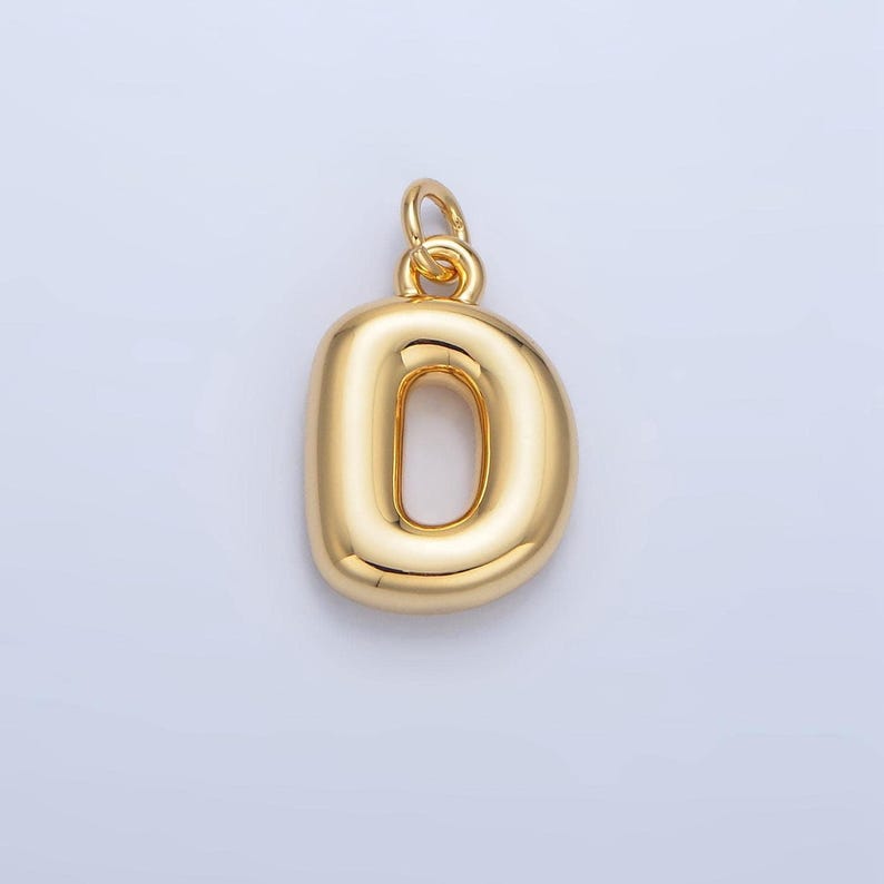 May include: A gold-colored charm in the shape of the letter D. The charm has a smooth, rounded surface and a hole at the top for attaching to a necklace or bracelet.