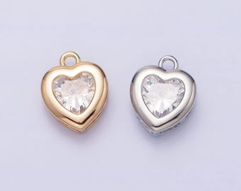 Puede incluir: Dos colgantes en forma de corazón con un cristal transparente en el centro. Un colgante es dorado y el otro plateado.