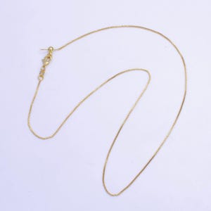 Puede incluir: Un collar de cadena de oro con cierre de caja. La cadena es fina y delicada.