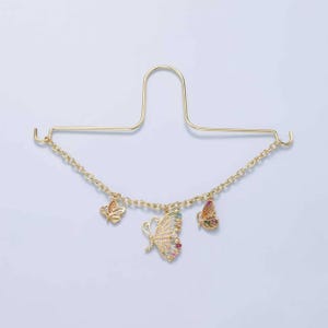 May include: Gold-toned metal bracelet with three butterfly charms. The butterflies are adorned with colorful gemstones. The bracelet is connected to a gold-colored metal hanger.