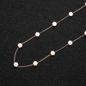 May include: A gold chain necklace with white hexagonal charms. The necklace is on a black background.
