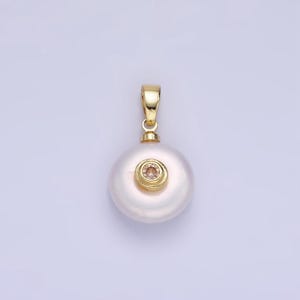 May include: A white pearl pendant with a gold setting and a small pink gemstone in the center.