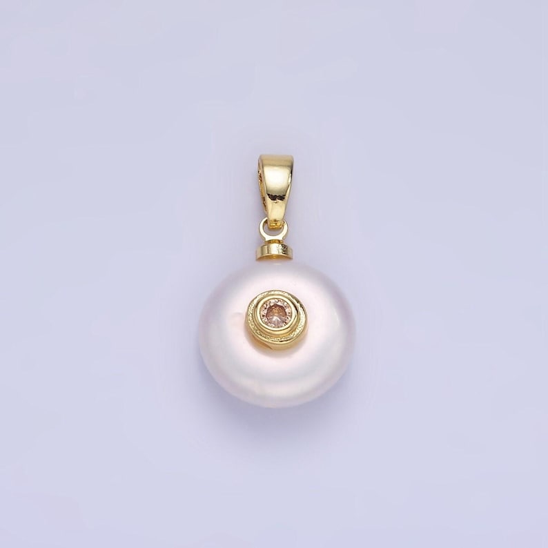 May include: A white pearl pendant with a gold setting and a small pink gemstone in the center.