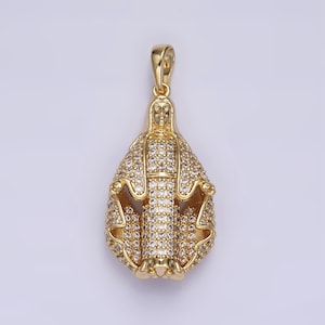 May include: Gold-toned pendant featuring a religious figure, encrusted with clear, sparkling stones. The pendant has a bail for a chain and is designed in a teardrop shape. The figure's face and hands are visible, adding detail to the jewelry.