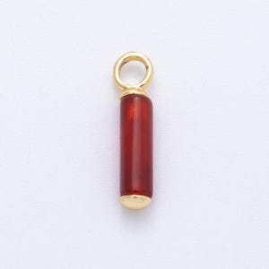 May include: A pendant with a cylindrical, translucent, deep red stone and gold-coloured metal accents. It has a small loop for a chain at the top and a gold cap at the bottom. The pendant is set against a white background.