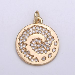 Puede incluir: Colgante de tono dorado con un diseño circular con un patrón de espiral de diamantes de imitación transparentes.