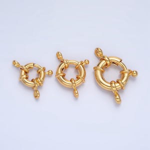 Pode incluir: Três fechos de anel de metal dourado de diferentes tamanhos. Cada fecho tem uma forma circular com um design de nó decorativo e três laços.
