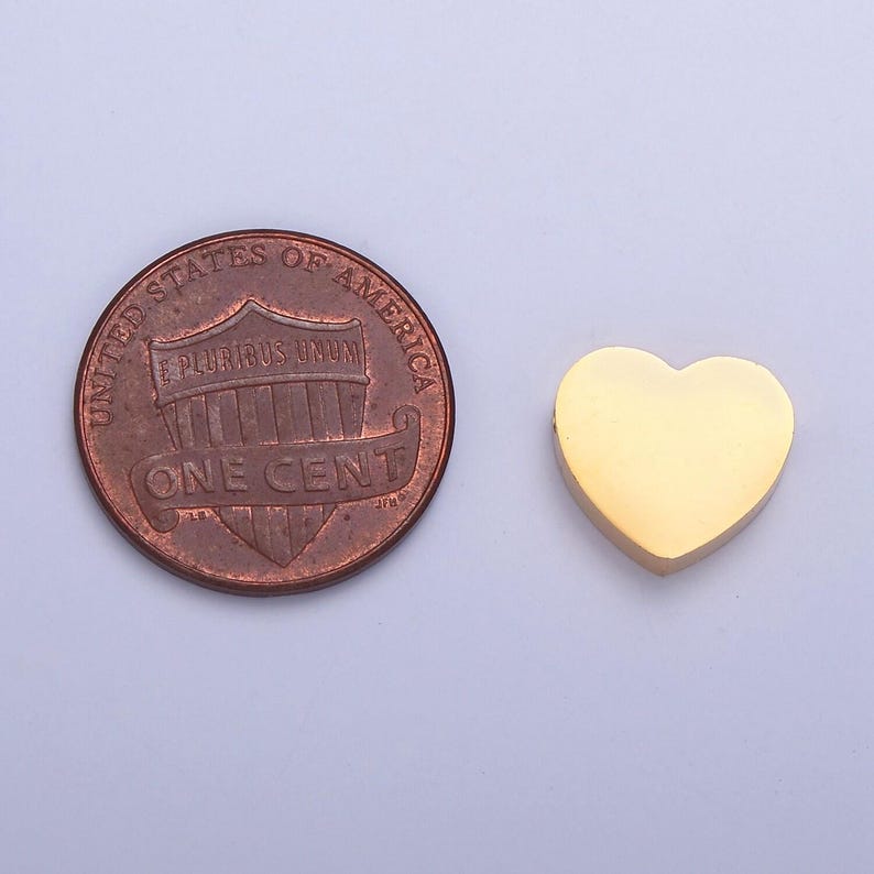 Puede incluir: Un dije de coraz&oacute;n de oro se muestra junto a un centavo estadounidense para comparar el tama&ntilde;o. El coraz&oacute;n es s&oacute;lido y tiene un acabado liso y brillante.