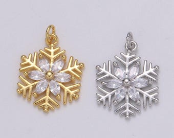 Könnte beinhalten: Zwei Schneeflocken-Anhänger, einer goldfarben und einer silberfarben. Jeder Anhänger hat ein zentrales Blumendesign mit klaren, facettierten Steinen. Das Schneeflocken-Design hat detaillierte, spitze Kanten und eine kleine Schlaufe.