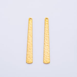 May include: Two gold-coloured, textured bar-shaped earring components. Each component has a small hole at the top for attachment. The bars have a hammered texture and a slightly tapered shape, wider at the bottom and narrower at the top.