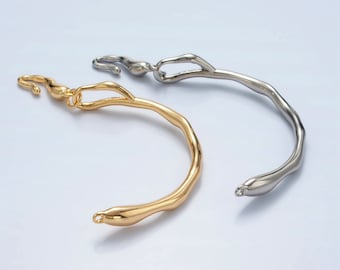 May include: Two abstract, organic-shaped bracelets. One is gold-toned, the other silver-toned. The bracelets have a flowing, irregular design, with a hook and loop closure. The jewellery is displayed on a light background.