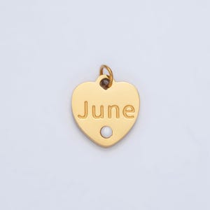 May include: Gold heart-shaped charm with the word "June" engraved on it. A small white pearl is centered on the charm.