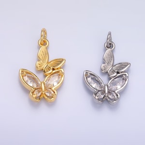 May include: Two butterfly pendants, one gold-toned and one silver-toned. Each pendant features two butterflies, one larger with clear crystal accents and a smaller one above. The pendants are designed for jewelry making.
