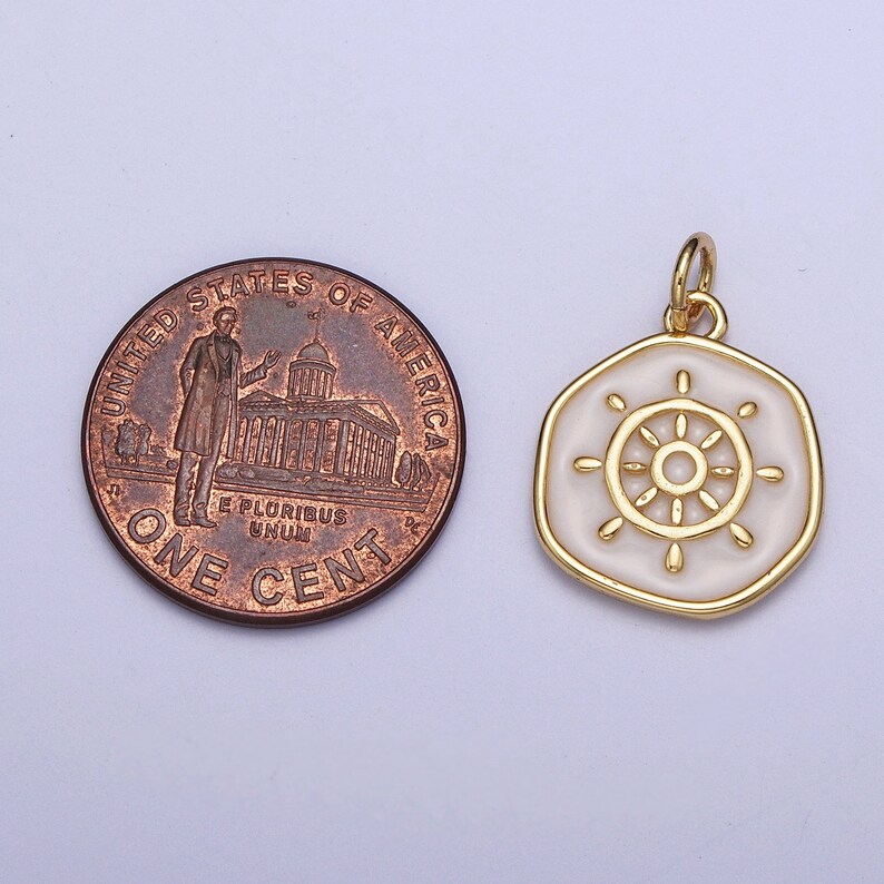 K&ouml;nnte beinhalten: Goldfarbener Anh&auml;nger mit wei&szlig;em Emaille-Steuerraddesign. Der Anh&auml;nger ist sechseckig mit einem goldenen Rand. Eine Ein-Cent-M&uuml;nze liegt neben dem Anh&auml;nger zum Gr&ouml;&szlig;envergleich. Der Anh&auml;nger hat eine kleine Schlaufe f&uuml;r eine Kette.