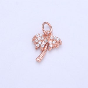 May include: A rose gold palm tree charm with clear crystal accents. The charm has a loop at the top for attaching to a bracelet or necklace.