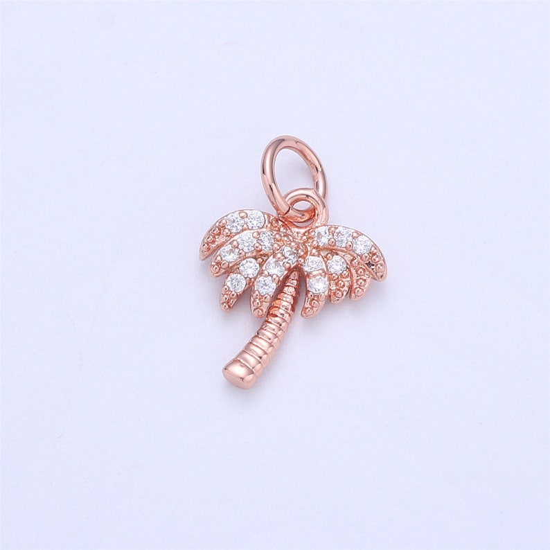 May include: A rose gold palm tree charm with clear crystal accents. The charm has a loop at the top for attaching to a bracelet or necklace.