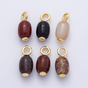 Puede incluir: Seis colgantes de piedras preciosas con detalles dorados. Los colgantes tienen forma ovalada y presentan una variedad de colores, incluyendo rojo, negro y beige. Cada colgante tiene un lazo dorado en la parte superior y una tapa dorada en la parte inferior.