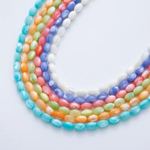 May include: A close-up of several strands of colorful oval-shaped beads. The beads are in shades of blue, green, yellow, orange, pink, and white. The beads are arranged in a curved pattern against a white background.