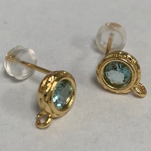 May include: A pair of gold earrings with a light blue gemstone in each. The earrings have a small loop on the bottom.